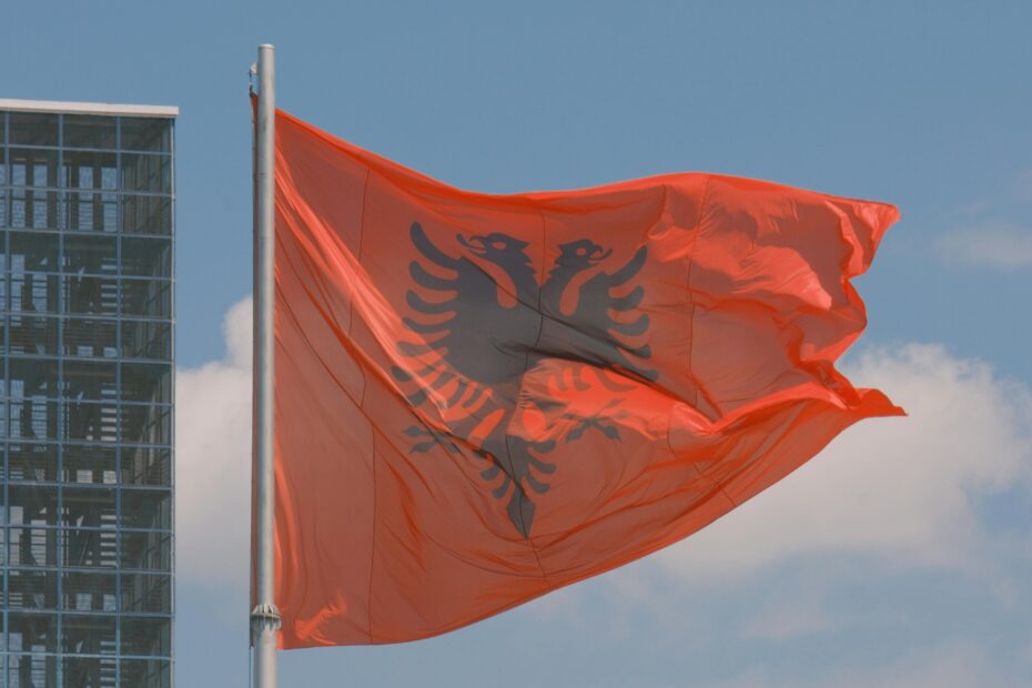 Albanian flag waving against a modern city backdrop, symbolizing national pride.