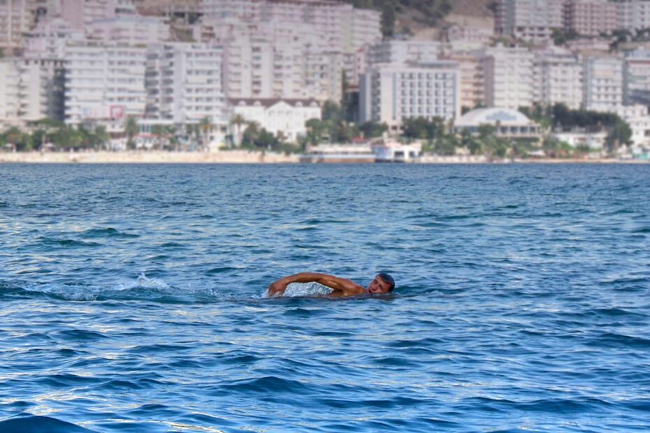 Man swimming in the Adriatic Sea with Sarandë, Albania skyline.