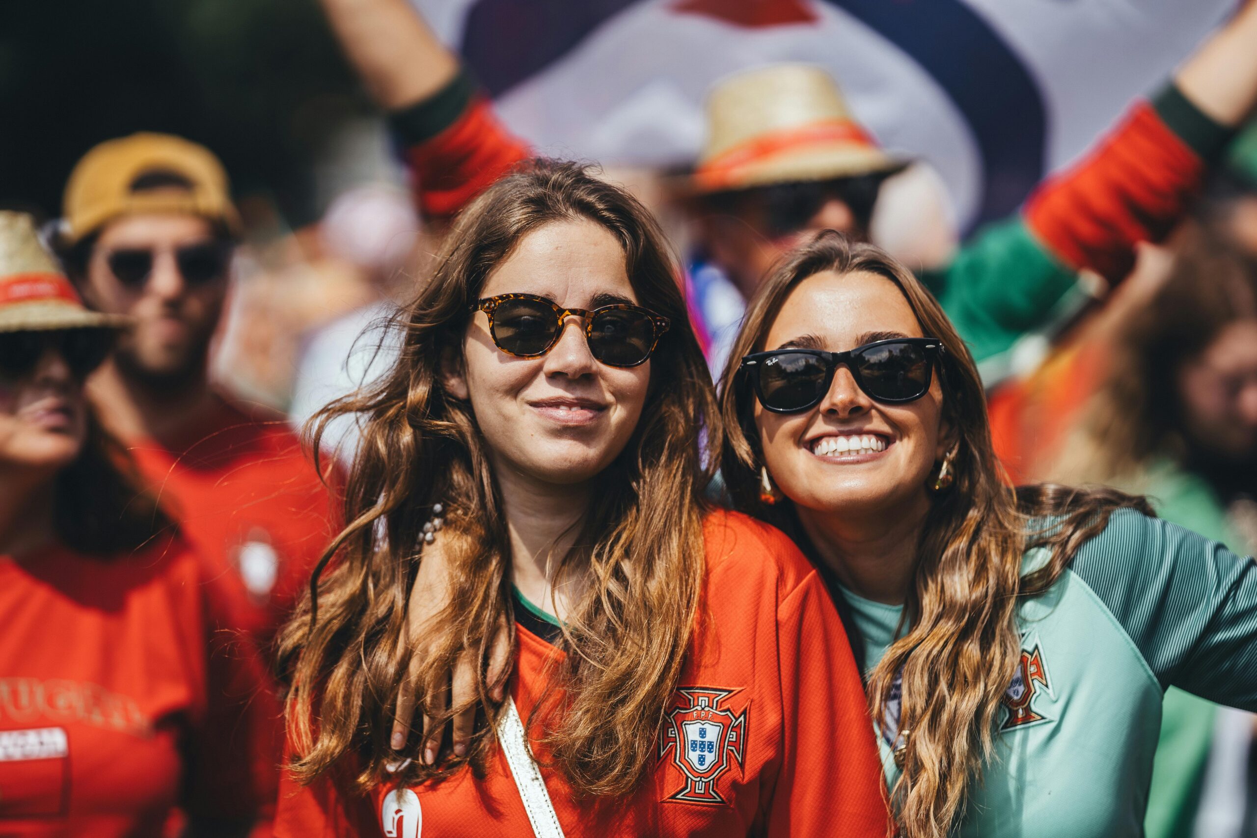 Two women in sunglasses cheering at an outdoor sports event, exuding happiness and excitement.