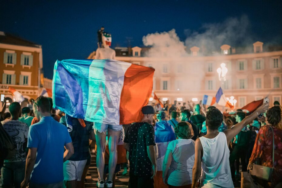 Vivid night-time celebration in France with crowds waving flags in city square.