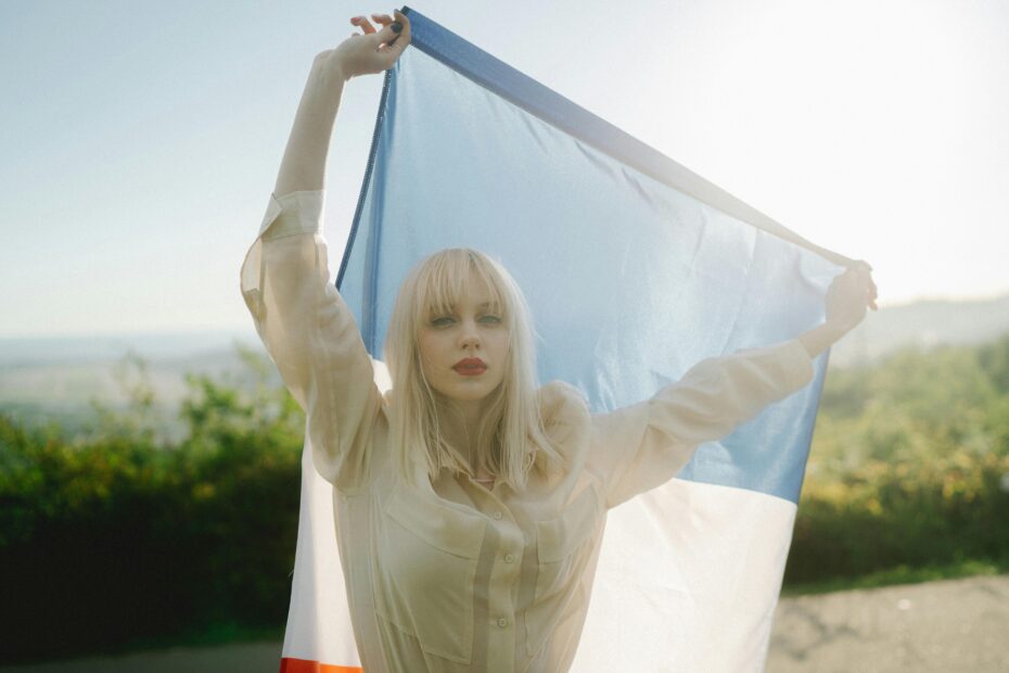 A woman holding a French flag outdoors with sunlight in the background, evoking freedom and patriotism.