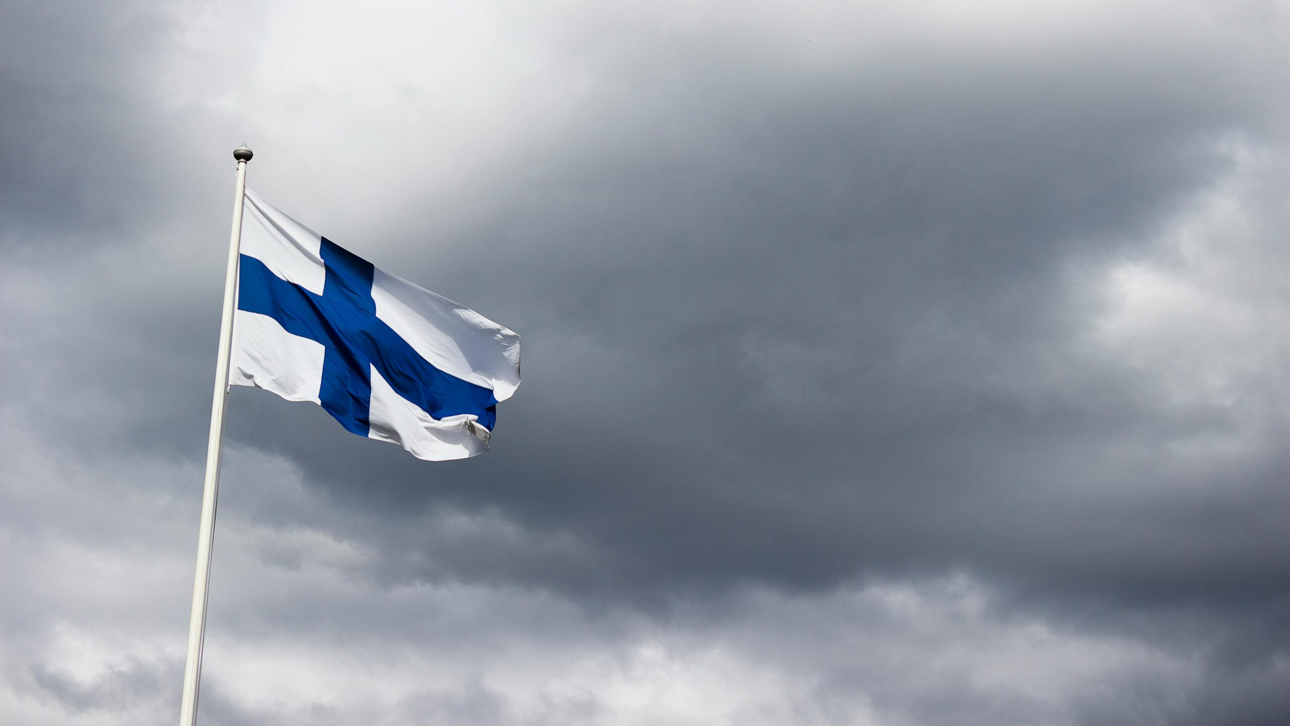 The Finnish flag waves proudly against a dramatic, cloudy sky, symbolizing national identity.