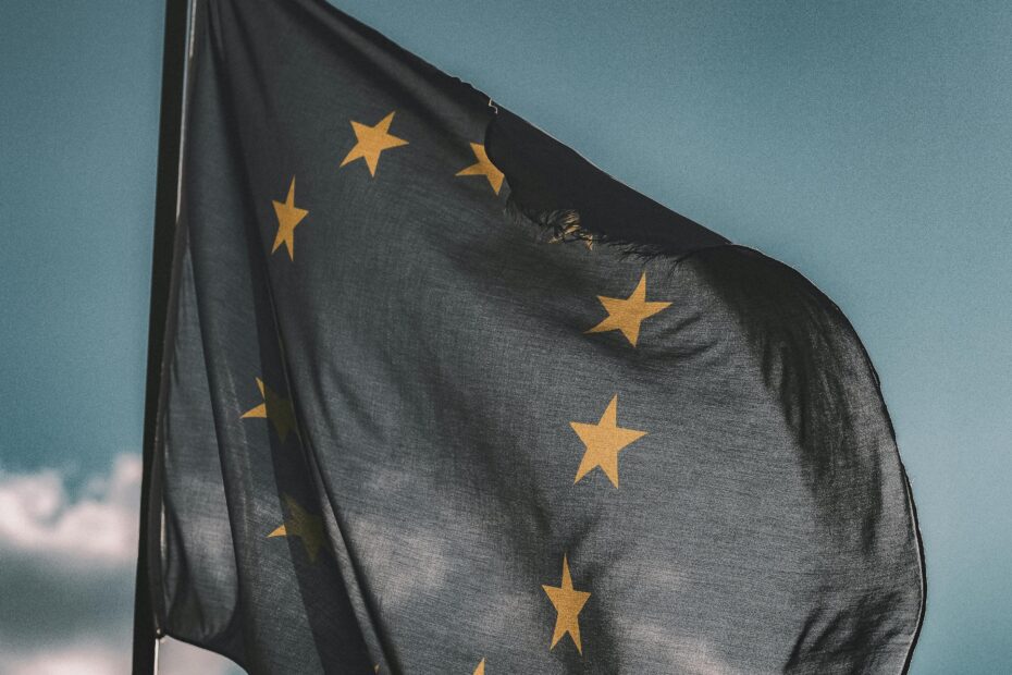 European Union flag gently waving on a flagpole against a cloudy sky, symbolizing unity and patriotism.