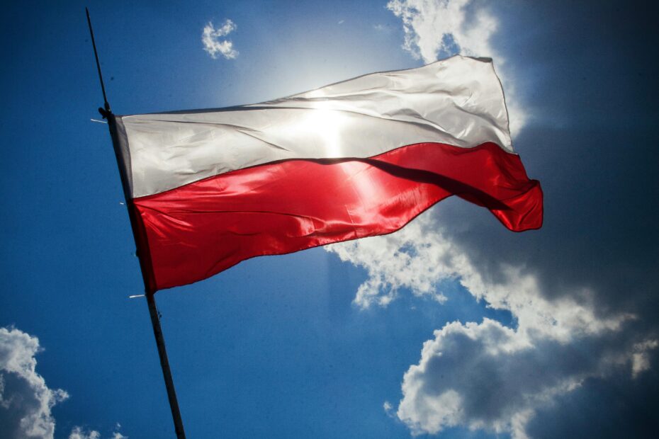 A Polish flag flutters against a bright blue sky with clouds, symbolizing national pride.