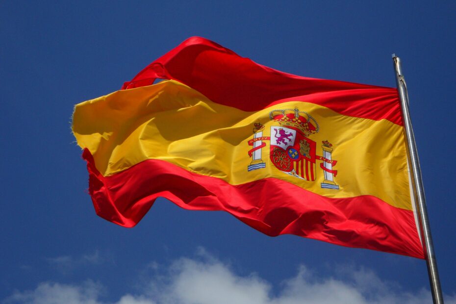 Vibrant Spanish flag waving against a clear blue sky and clouds.