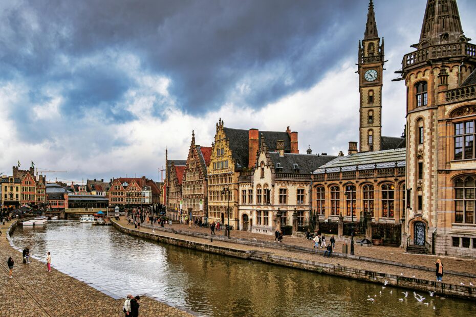Charming view of Ghent's historic architecture along the water under dramatic skies.