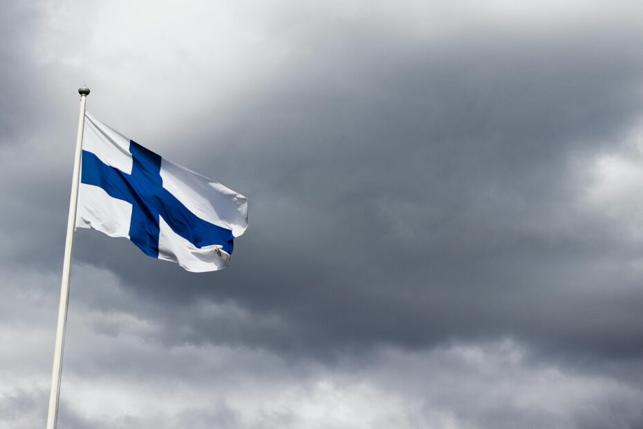 The Finnish flag waves proudly against a dramatic, cloudy sky, symbolizing national identity.
